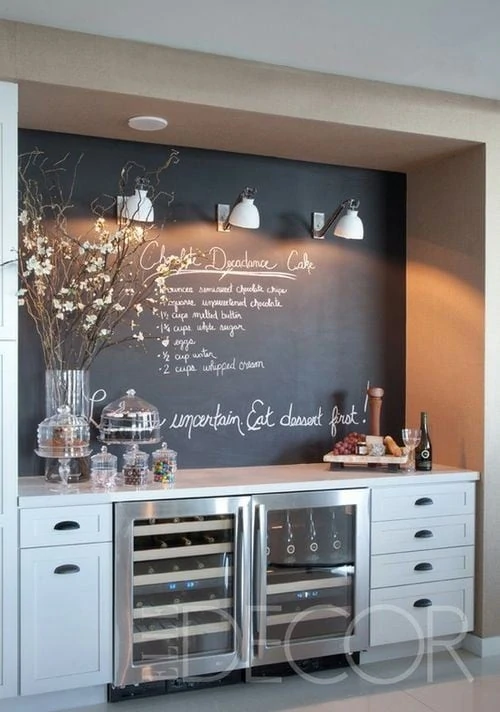 A chalkboard with writing on it, lights on the board and a small side table with cakes on it.