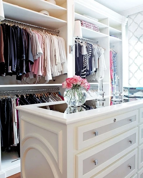A white closet with a white closet island and pink flowers in a clear vase on it.