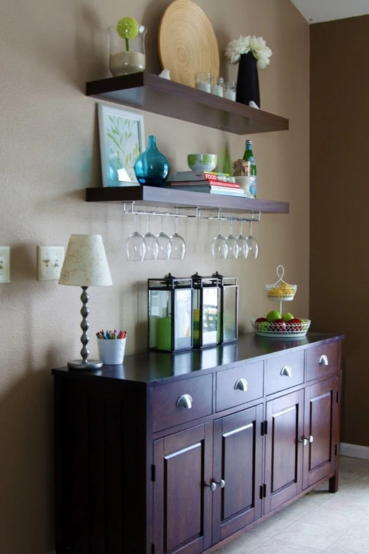 A hutch with a bar shelf over top of it, a lamp on the hutch and wine glasses hanging from the shelf.