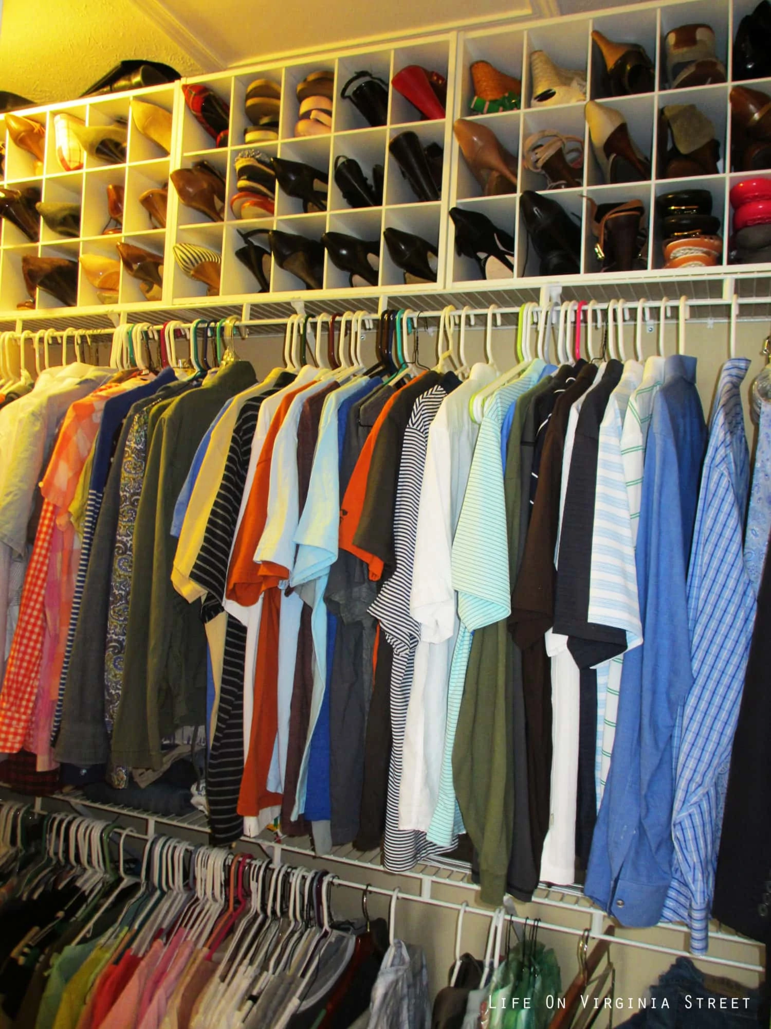 A close up picture of the shirts and shoes in the closet.