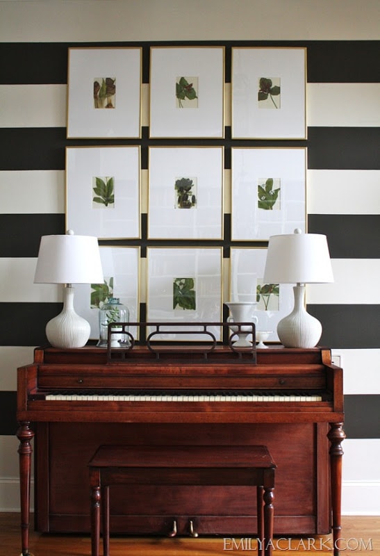 Black and white striped walls with a wooden piano in front of it.