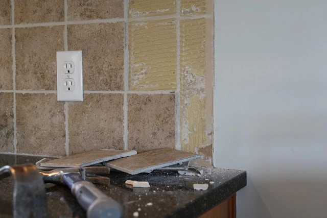 Removing ceramic tile backsplash with a hammer on the counter.