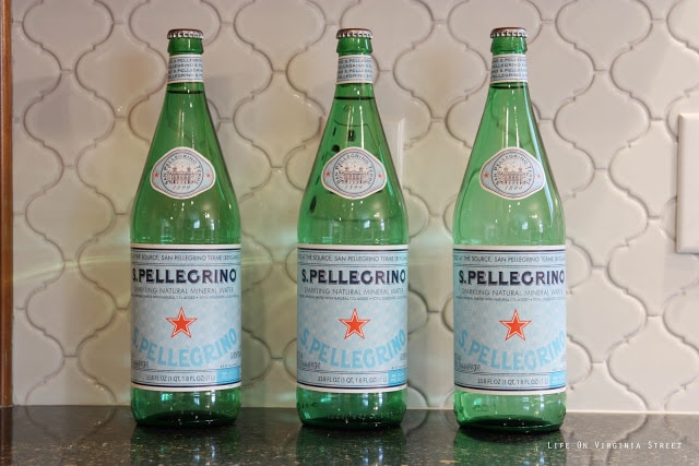 White Moroccan Tile backsplash in kitchen with 3 green glass bottles in front of it.