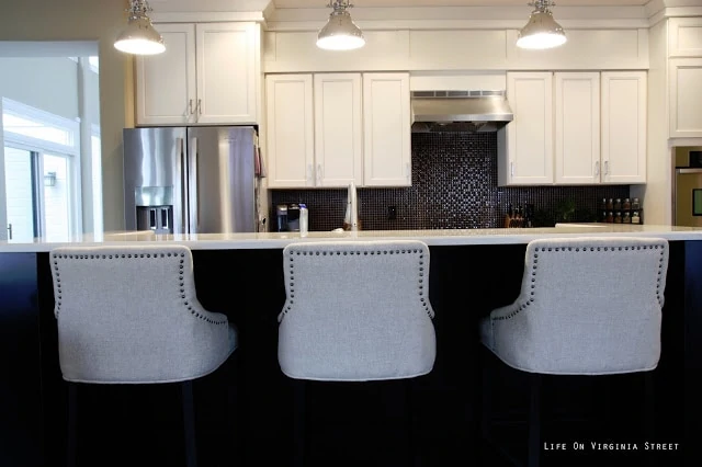 Linen barstools in a kitchen with white cabinets and a black island