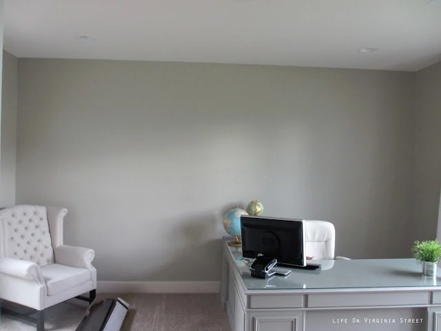 An empty room with a blank wall and a white chair in the corner of the room.