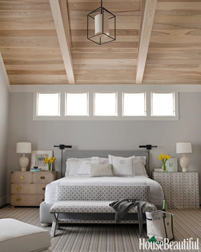 Wood beams on the ceiling, gray bed, gray walls, and side table with lamps on them.