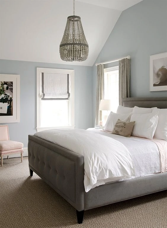 Gray blue walls, gray bed with white bedding and a wooden chandelier above bed.