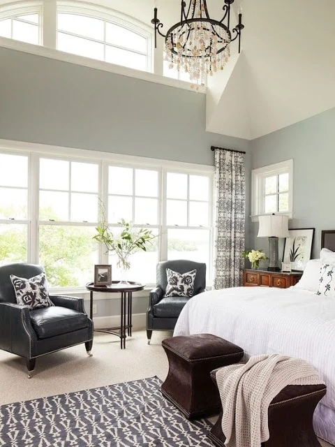  Large, full-wall windows, rustic black chandelier above bed, gray and green on walls.