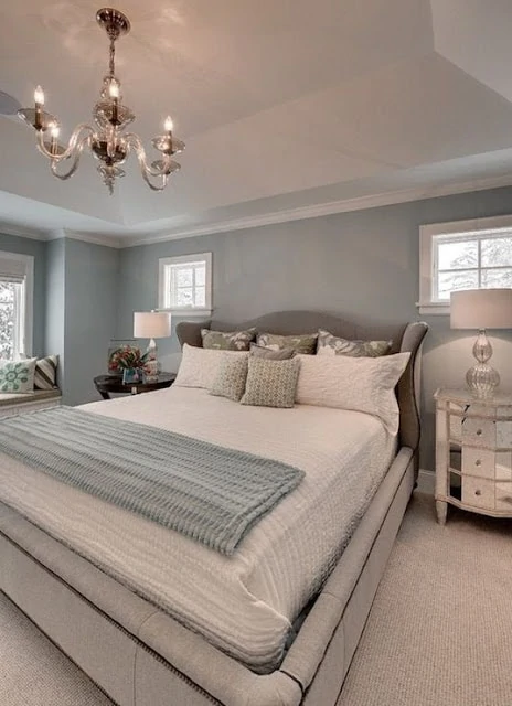 Blue gray bedroom wall color with white trim and chandelier above bed.
