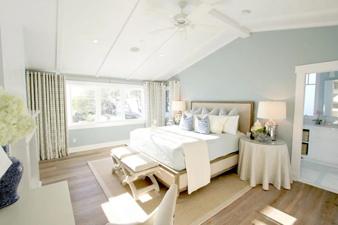 Turquoise green room, light beige bed, side table with beige tablecloth, and footstools at the head of the bed.