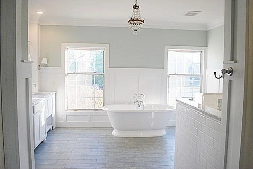 White bathroom with a hint of green on the walls and a chandelier above the stand alone bathtub.