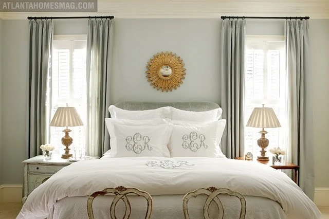 A mix of green, blue, and grey undertones come together in this master bedroom. There is a gold sunburst mirror above the bed.