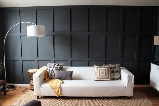 Dark board and batten wall with a couch and geometric shapes on pillows. 