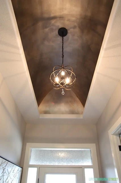 A orb chandelier up high in the hallway of a house.