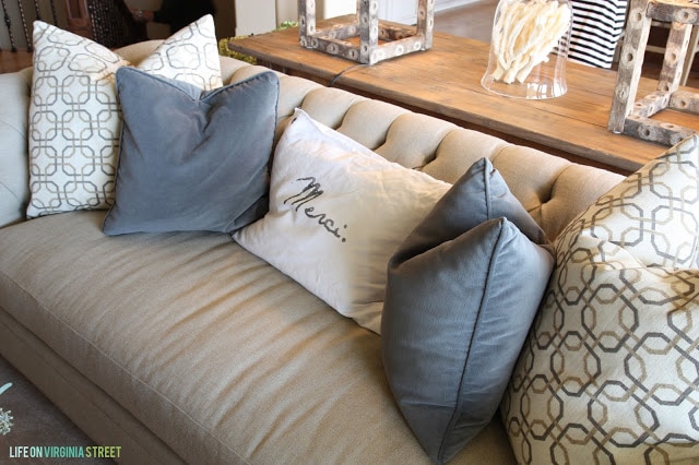 Tan couch with blue-gray and Merci pillows.