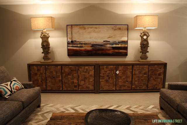 Basement living room with a wooden console, two lamps and brown sofas.