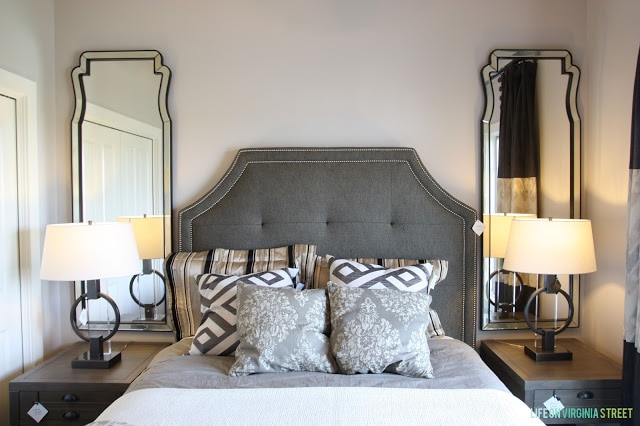 A bed flanked by two side tables and two mirrors above the tables.