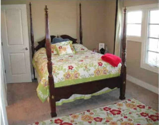 A four poster wooden bed with floral bedspread and floral rug.