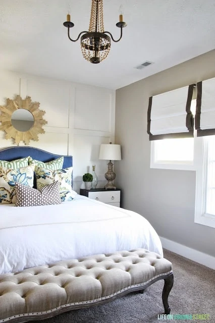 Wooden chandelier, white bedspread, blue headboard and nightstand with a lamp in the guest bedroom.