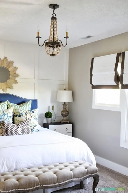 Guest bedroom with a wood bead chandelier, blue headboard, white bedding, and a linen and oak bench.