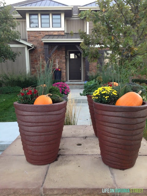 Large planter filled with flowers and pumpkins in front of house.