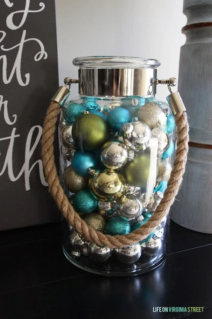 A clear glass jar filled with blue, green and silver ornaments.