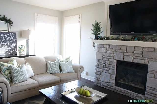 Neutral couch, coffee table with fruit on it and a large fireplace in living room.