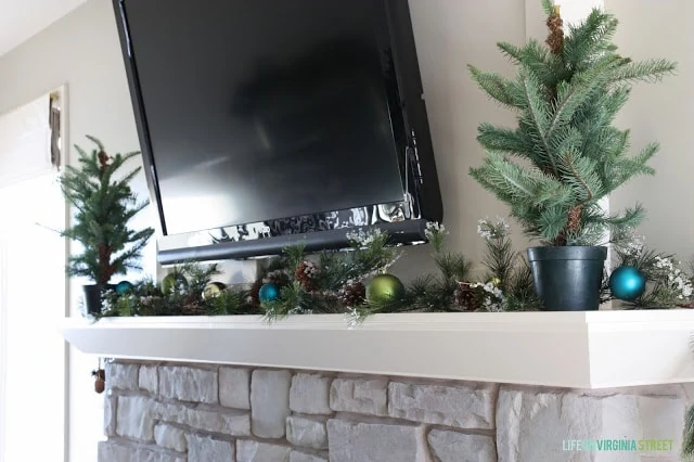 Stone fireplace mantel with green pine branches on it and decorations.