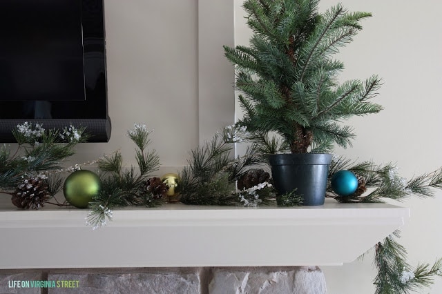 Fireplace mantel with mini tree in pot on it and holiday decorations.