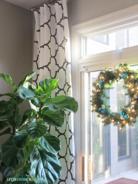 A green plant, black and white curtains and a wreath on the window.