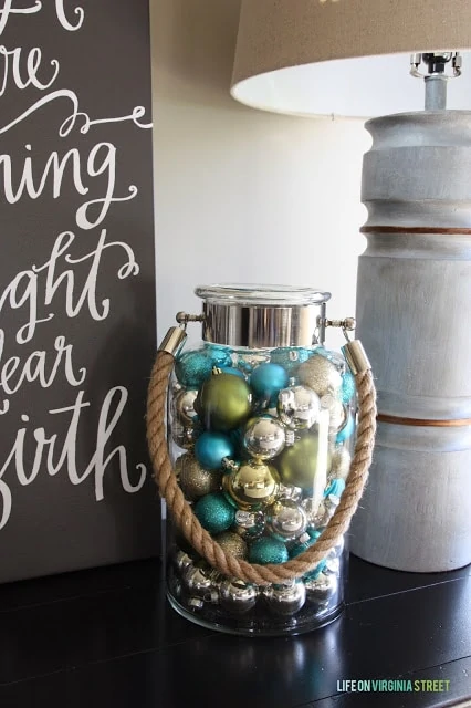Multi colored ornaments in a glass jar with rope as a carrying handle.