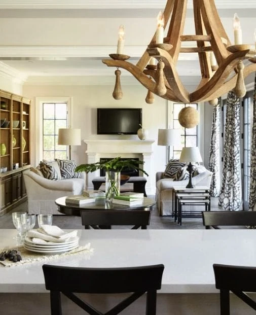 Wooden chunky chandelier above dining room table that is white with dark brown chairs.