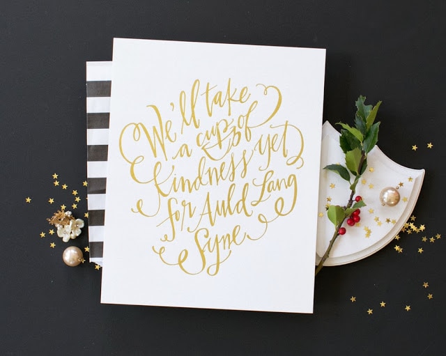 Auld Lang song saying on paper with glitter and holly beside it.