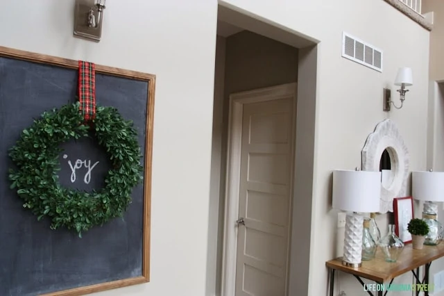 There is a chalkboard in the entryway with a wreath on it and the word joy written on the chalkboard.