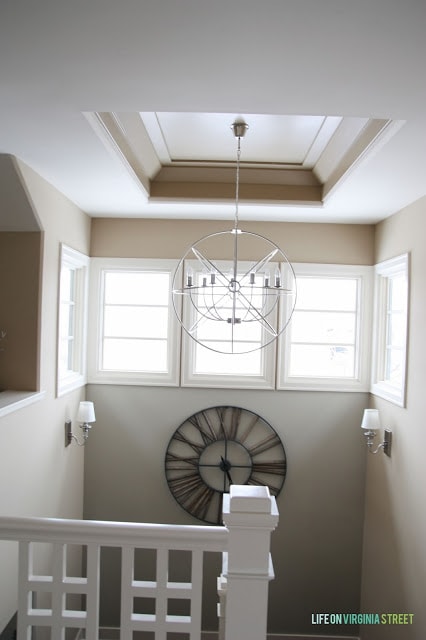 There is a clock on the wall by the new chandelier.