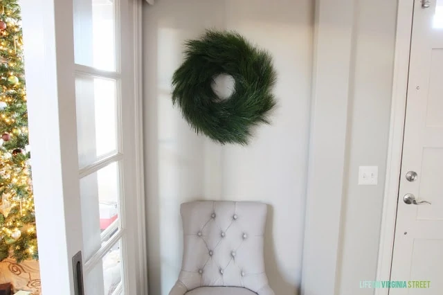 Green wreath hanging in room with large window and a chair underneath it.