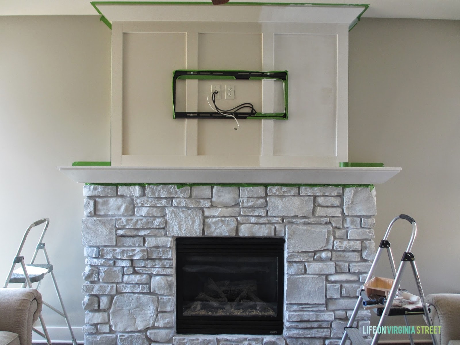 The fireplace with the TV not yet mounted but the wires there. Also green painters tape around the fireplace.