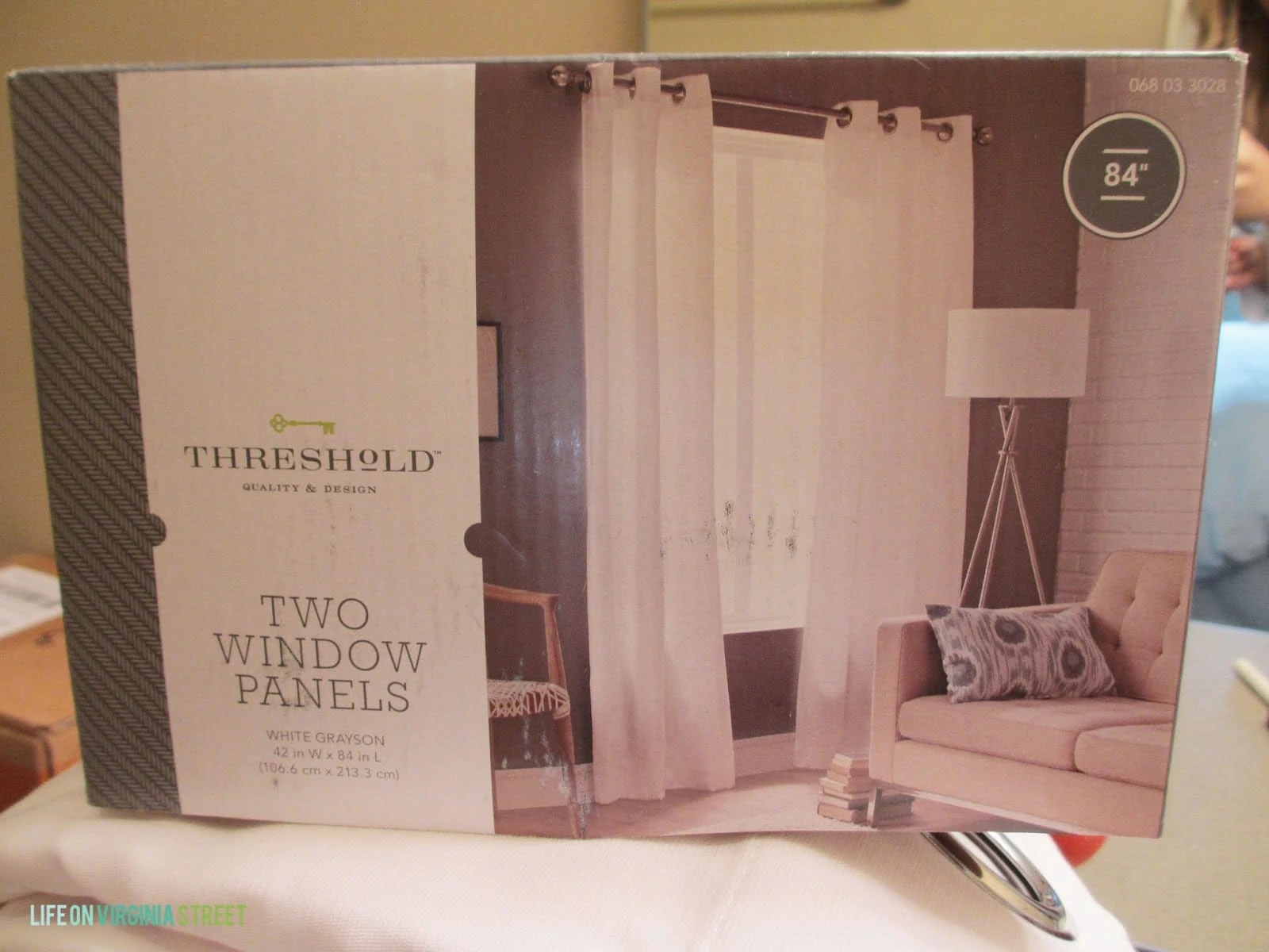 Plain white window panel curtain shown in a box.