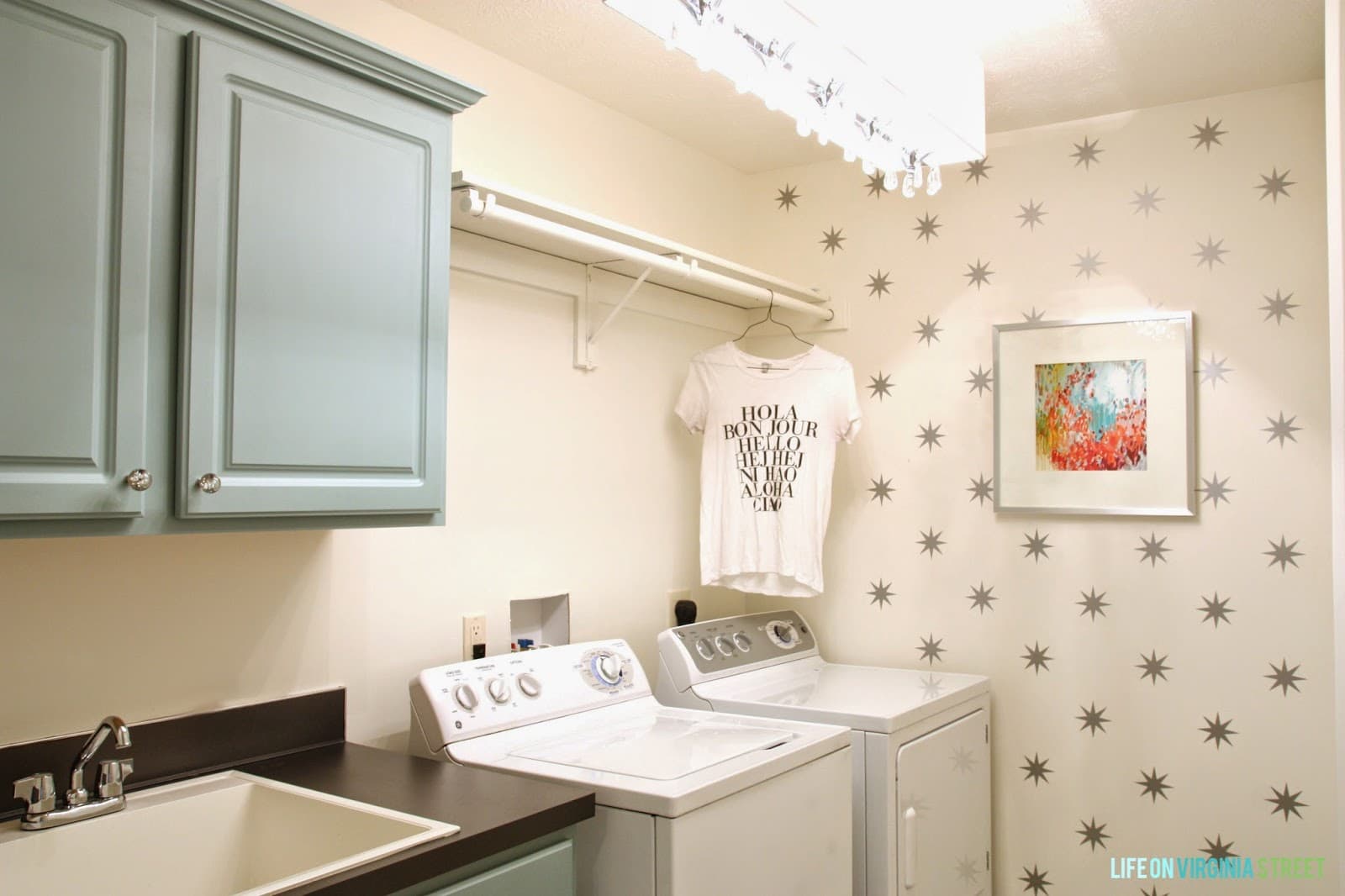 White laundry room with star decals, aqua cabinets, striped rug and colorful art.