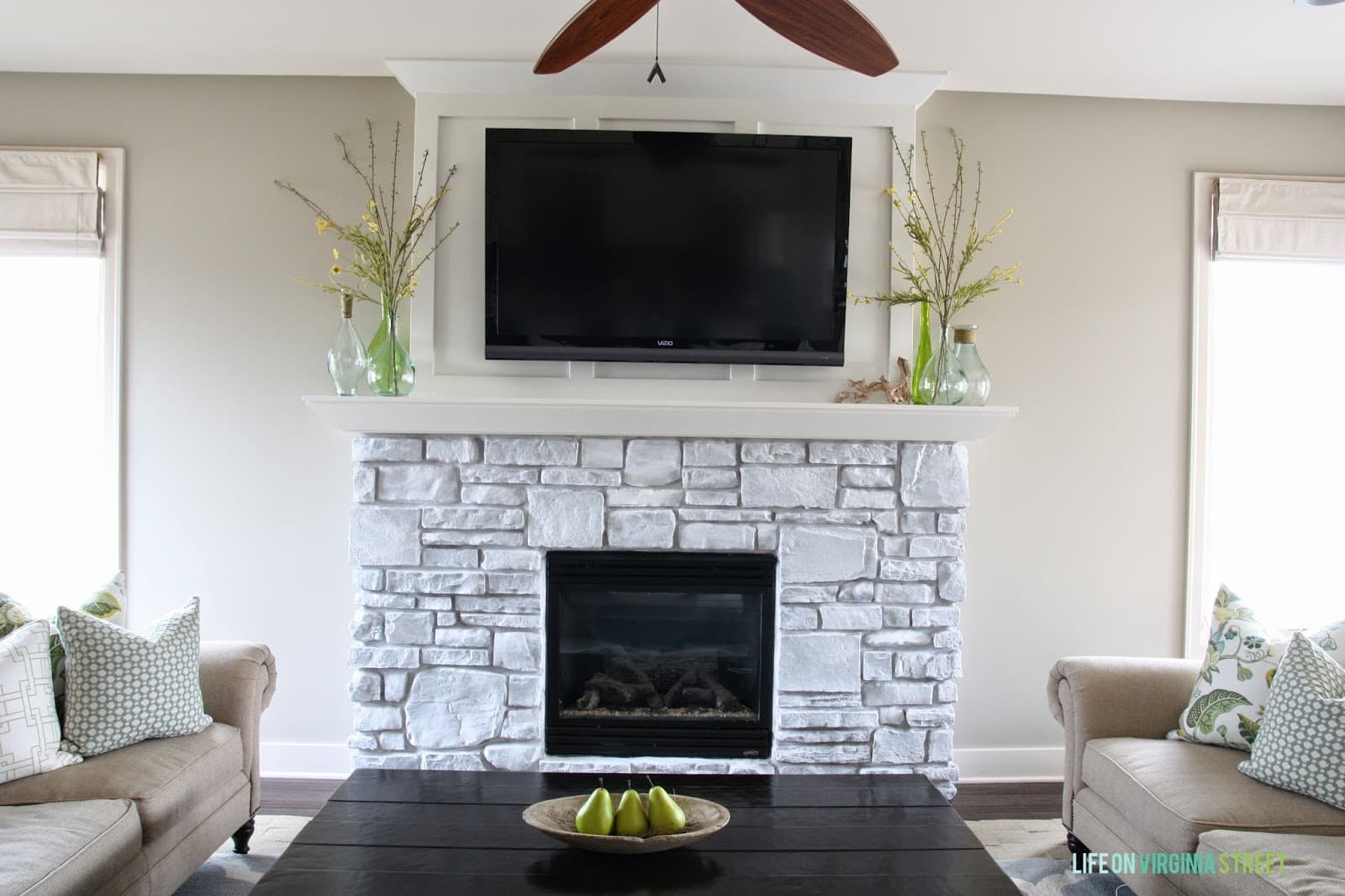 A whitewashed stone fireplace with board and batten feature wall, and two vases on the fireplace.