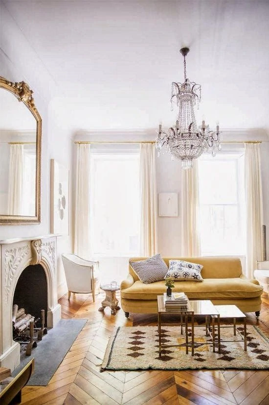 A light apartment in Parisian style with an ornate fireplace, a mirror above the fireplace, and a chandelier in the room.