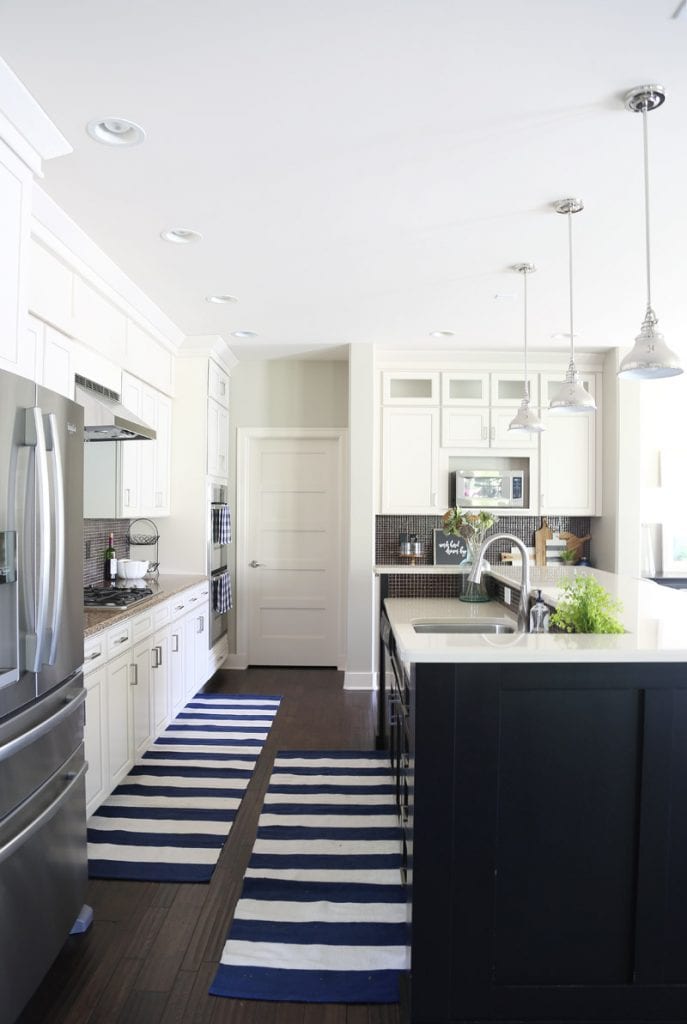 white-kitchen-cabinets-with-black-island-and-navy-striped-rug-via-life-on-virginia-street