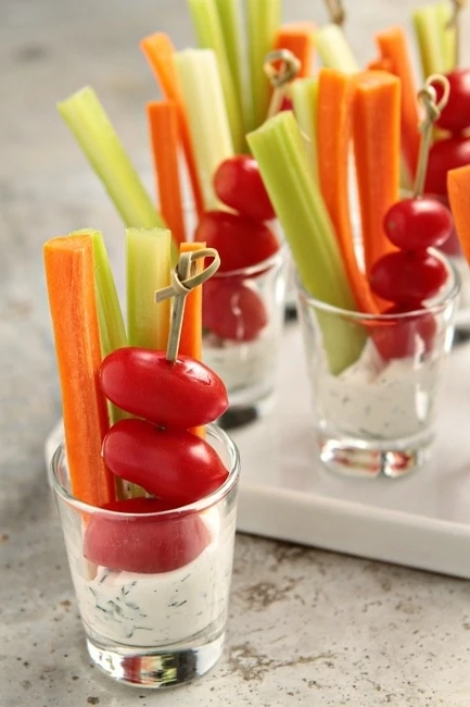 A clear glass with vegetables and dip in it.