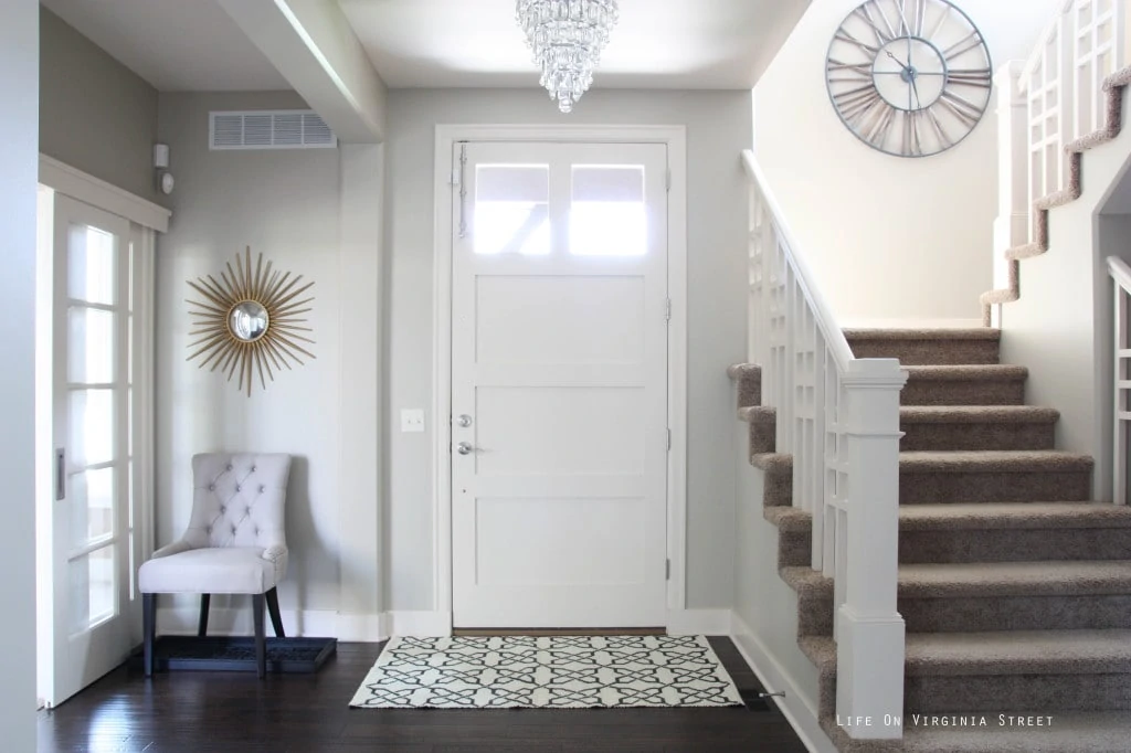 Light and bright ntryway with Behr Castle Path walls and Behr Elephant Skin Door. There is a chandelier hanging up in the hallway as well.