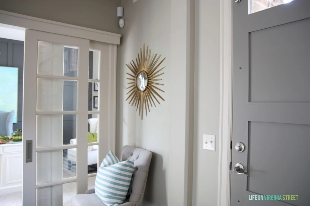 A gold sunburst mirror is on the wall above the chair in the hallway.