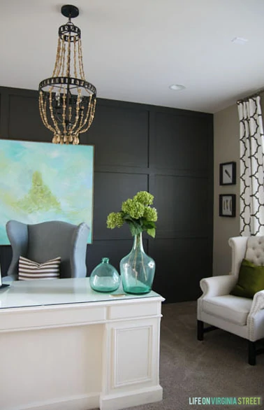 Office with dark gray walls and a wood chandelier, with glass vases filled with green hydrangeas.