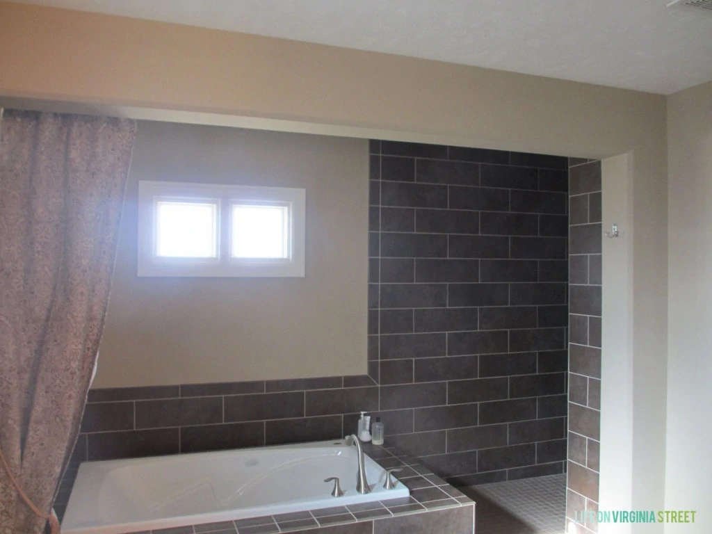 A side view of the tub with dark tiles, and a small window above the tub.