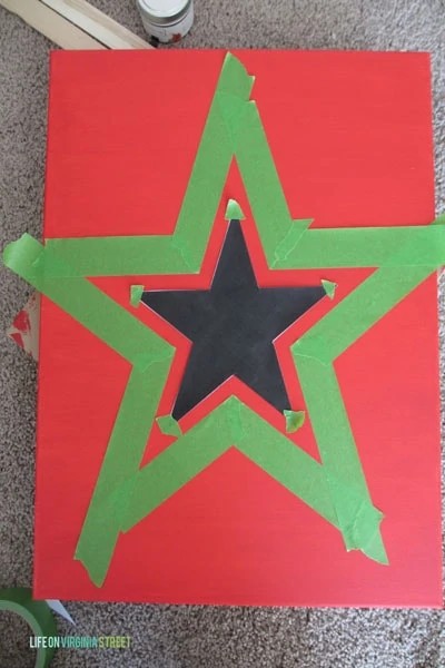 The star being outlined with green painters tape on red cardboard.