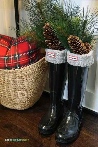 Cute Christmas entryway decor idea with boots filled with holiday greenery.