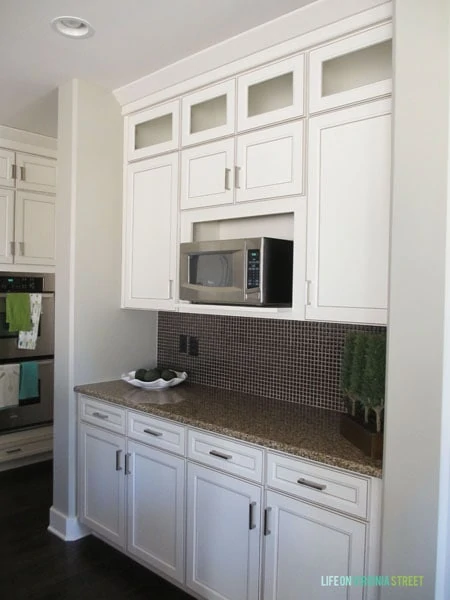 A white kitchen with dark counters and a built in microwave.